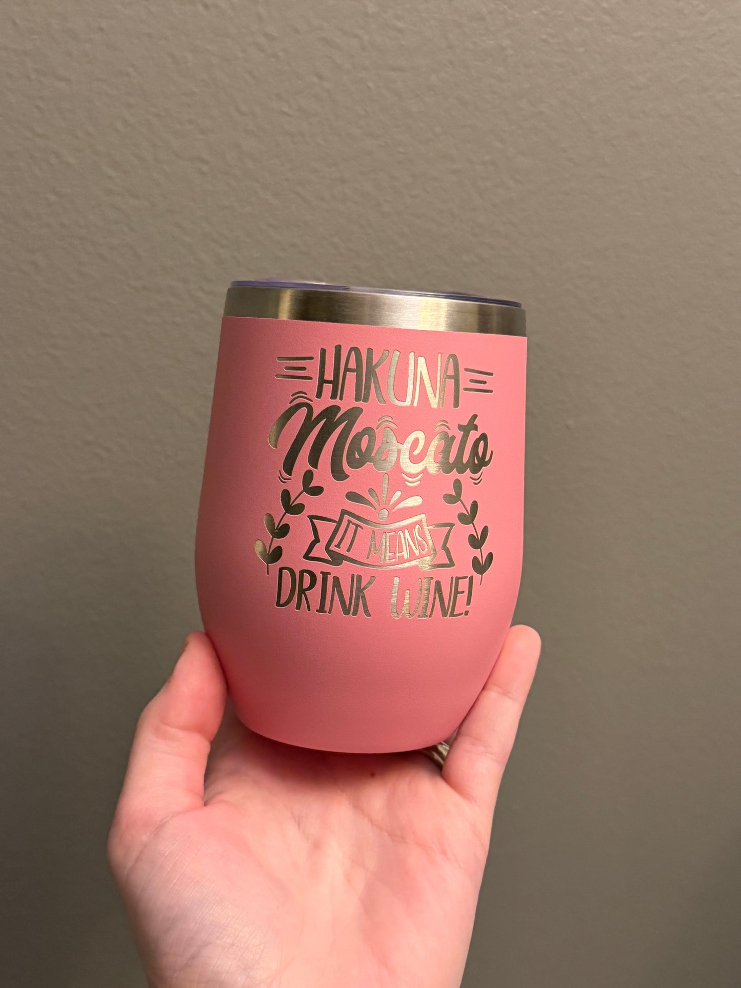 Pink tumbler with text held by a hand against a plain background