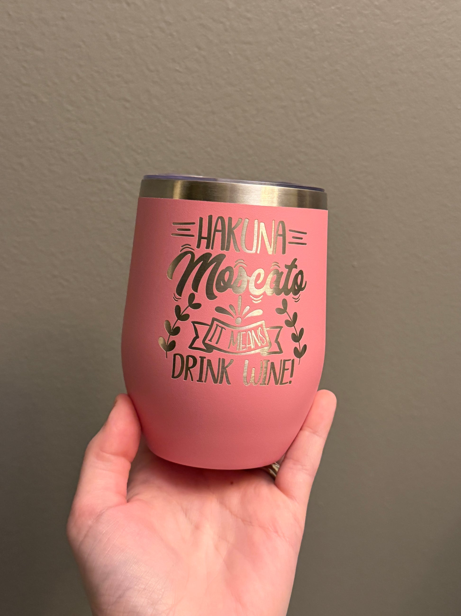 Pink tumbler with text held by a hand against a plain background