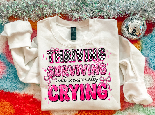 White sweatshirt with pink and black text on a colorful, textured surface with disco ball and tinsel.
