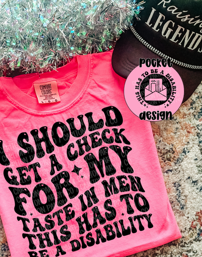 Pink t-shirt with black text and a tag on a textured surface.