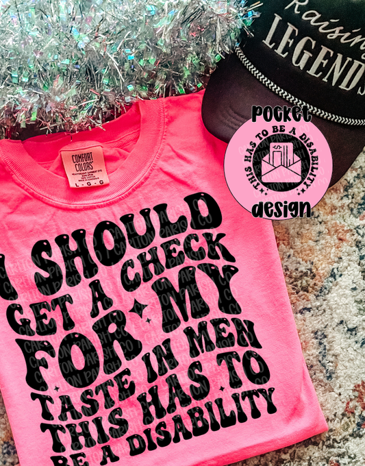 Pink t-shirt with black text and a tag on a textured surface.