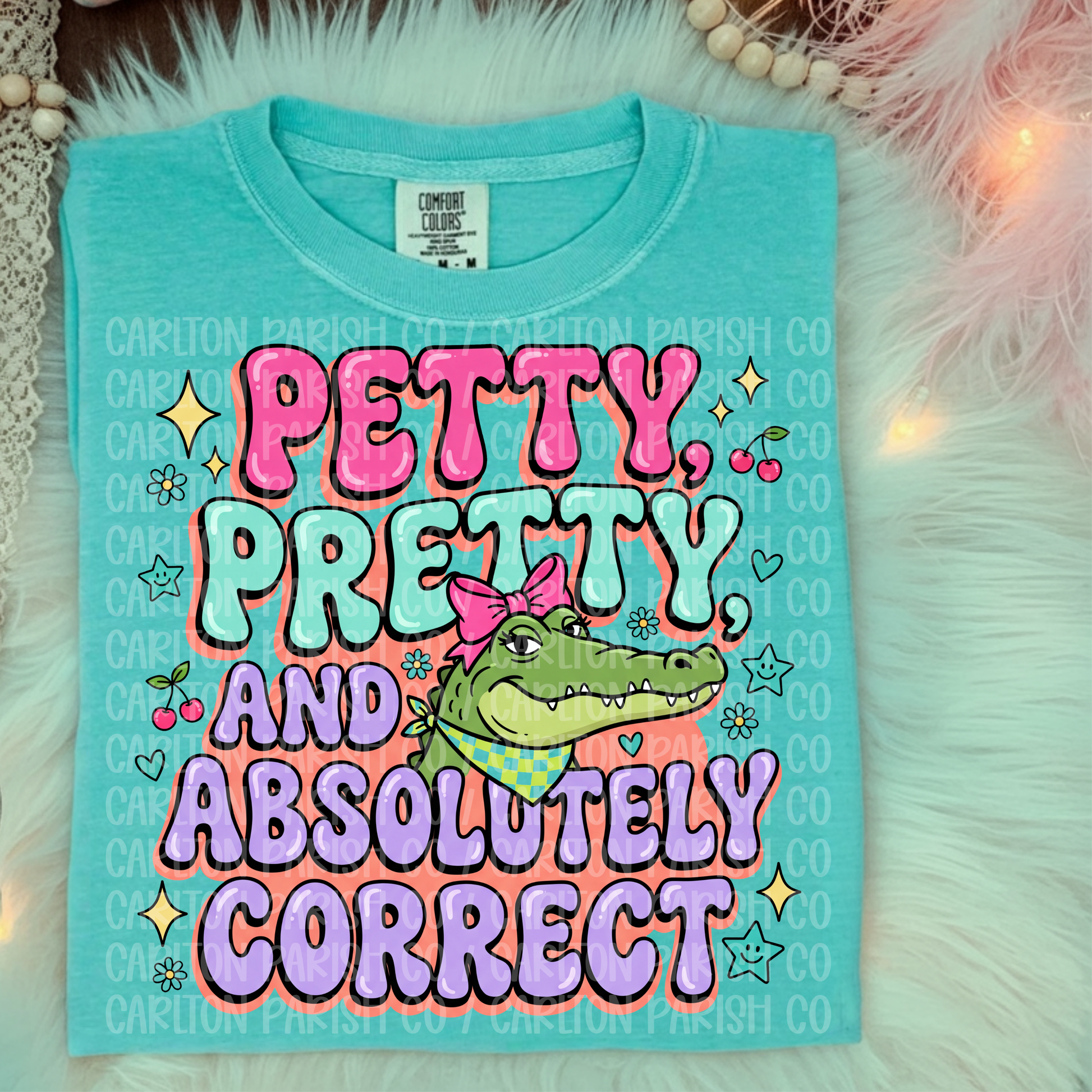 Turquoise t-shirt with colorful text and alligator graphic on a fluffy white surface.