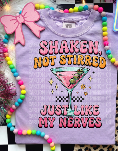 Purple t-shirt with cocktail graphic and text 'Shaken, Not Stirred Just Like My Nerves' on a colorful background.