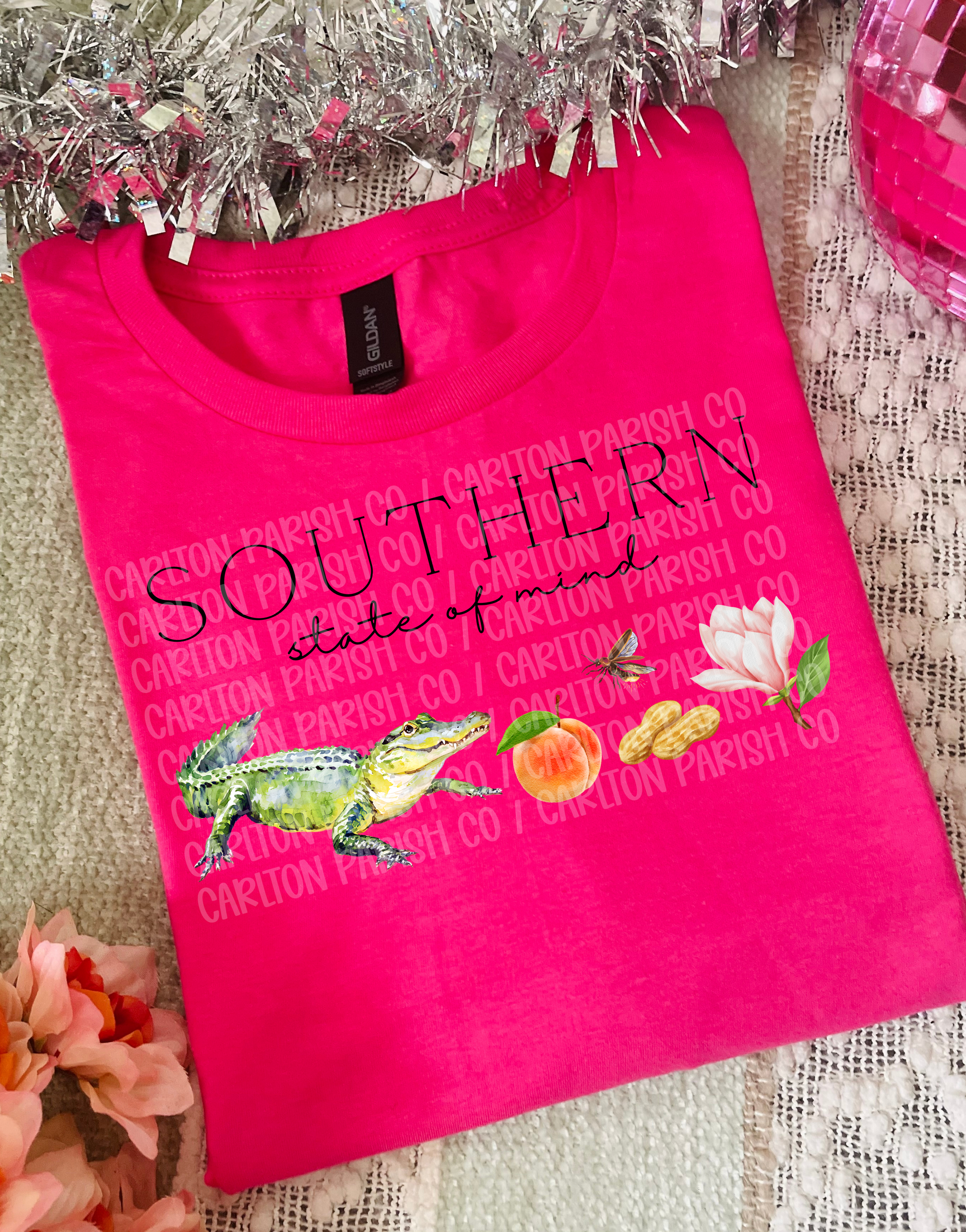 Pink t-shirt with 'Southern state of mind' text, frog graphic, and flowers on a textured surface.